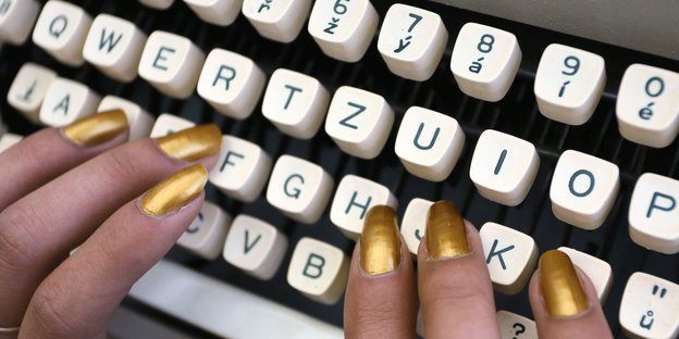 Goldenlackierte Finger tippen auf eine Schreibmaschine