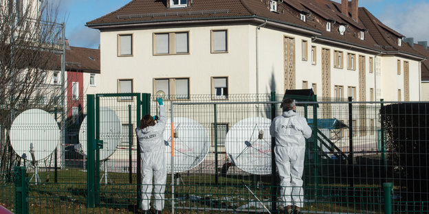 Kriminalbeamte in weißen Anzügen stehen vor einem Zaun