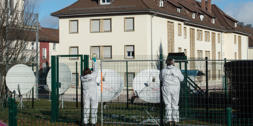 Kriminalbeamte in weißen Anzügen stehen vor einem Zaun