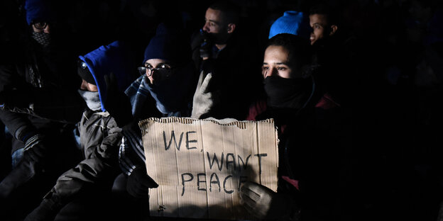 Flüchtlinge halten ein sTück Pappe hoch, auf dem steht: "We want peace".