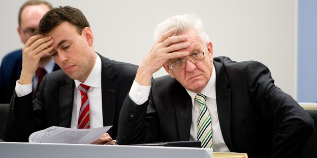Die baden-württembergischen Politiker Nils Schmid und Winfried Kretschmann sitzen nebeneinander und halten sich die Stirn.