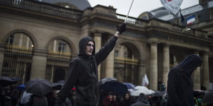 Ein Demonstrant hält eine Fahne hoch, im Hintergrund stehen weitere Menschen mit Regenschirmen