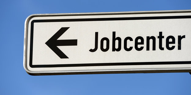 Auf einem Wegweiser steht „Jobcenter“ und ein Pfeil, der nach links zeigt.