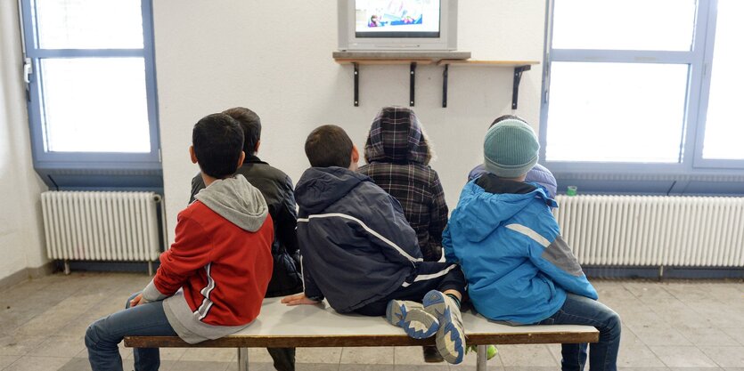 Kinder sitzen auf einem Tisch und schauen auf einen Fernseher