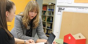Frau mit blonden Haaren erklärt einer Teenagerin am Laptop etwas Frau mit blonden Haaren erklärt einer Teenagerin am Laptop etwas