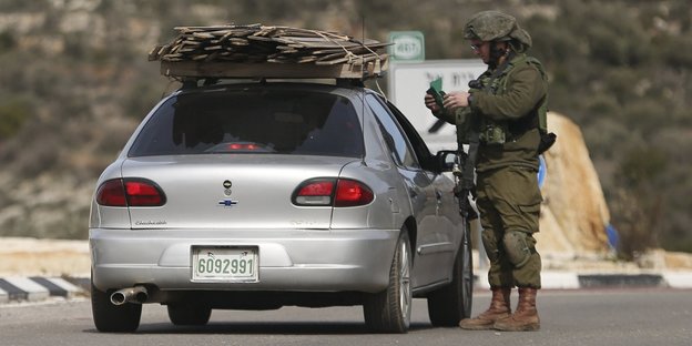 Ein Soldat steht neben einem Auto und sieht sich Dokumente an.