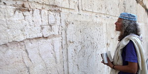 Eine Frau mit einem weißen Schal betet mit geschlossenen Augen an der Klagemauer in Jerusalem