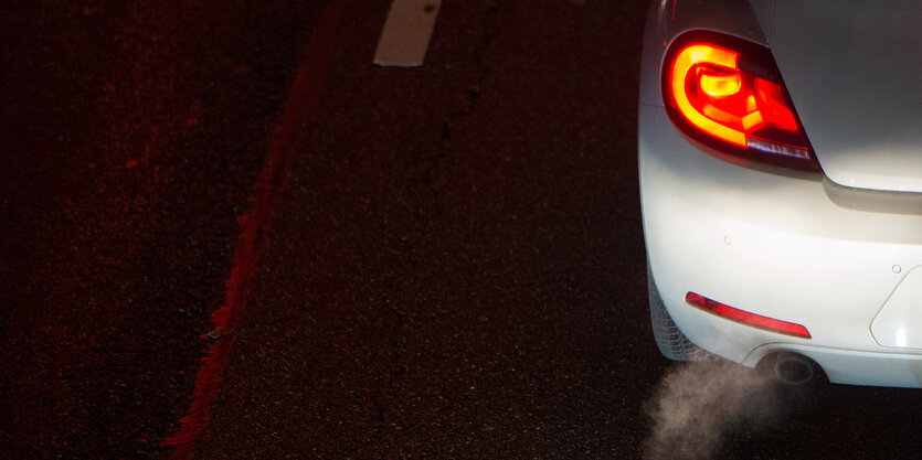 Von schräg oben gesehen: Auto in der Nacht mit Rücklicht und Abgasen aus dem Auspuff.