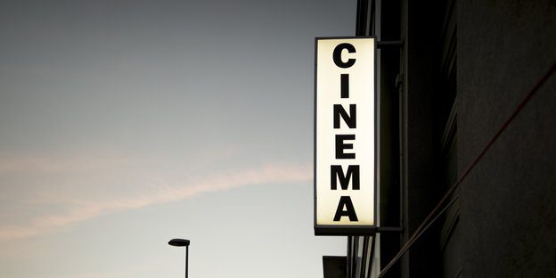 Eine Hauswand, daran das beleuchtete Wort Cinema, vor Abendhimmel