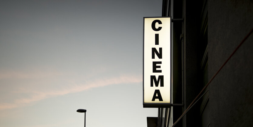 Eine Hauswand, daran das beleuchtete Wort Cinema, vor Abendhimmel