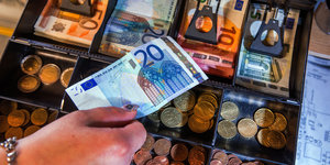 Hand mit 20-Euroschein über geöffneter Registrierkasse