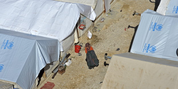 Eine Frau läuft in einem Flüchtlingscamp in Libanon zwischen großen Zelten entlang