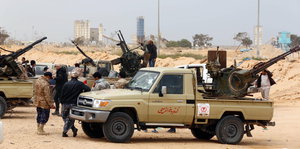 Mehrere Männer an Pick-up-Trucks mit schweren Waffen