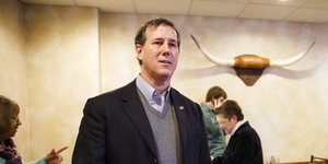 Rick Santorum steht in einem Raum. Hinter ihm an der Wand hängen Stierhörner, im Hintergrund einige Menschen