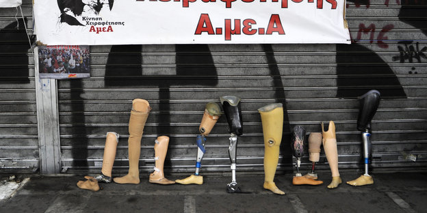 Ein knappes Dutzend Beinprothesen lehnen an einer graffitiverzierten Wand