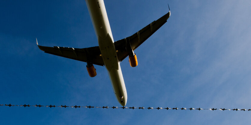 Ein Flugzeug fliegt über Stacheldraht.