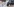 Mann kniet sich im Freien auf ein auf den Boden ausgebreitetes Banner mit Fotos nieder und küsst es.