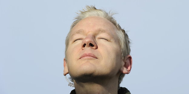 Julian Assange mit geschlossenen Augen vor blauem Himmel