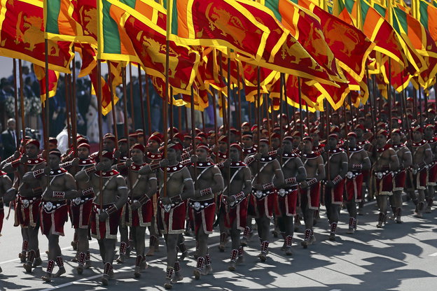 Männer in roten Röcken halten rot-gelbe Fahnen und marschieren in Formation