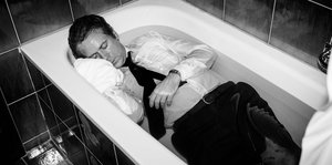 ein Mann liegt angezogen in einer gefüllten Badewanne