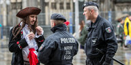 Ein Mann mit Piratenkostüm unterhält sich mit zwei Männern mit Polizeikostümen, im Hintergrund der Kölner Dom.
