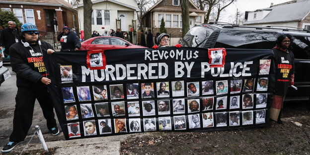 Menschen auf einer Straße halten ein Schild mit Portraitfotos in den Händen. Darüber steht in Englisch: "Getötet von der Polizeit".