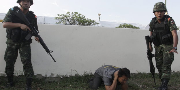 Zwei thailändische Soldaten bedrohen ein „Rothemd“ mit Schusswaffen.