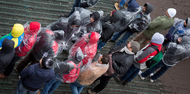 Menschen in Regenkleidung stehen in einer Schlange an.