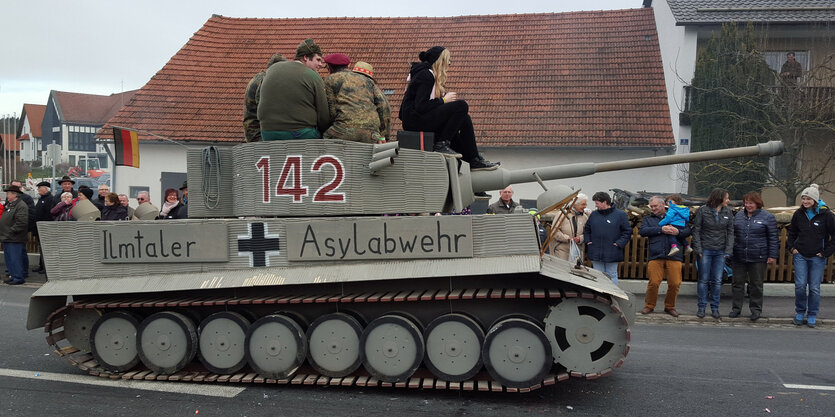 Ein Karnevals-Wagen in Gestalt eines Panzers mit der Aufschrift „Ilmtaler Asylabwehr“ fährt eine Straße entlang