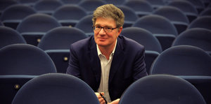 Ein Mann mit grauem Haar, Brille, offenem Sakko und Hemd sitzt in einem leeren Kinosaal. Es ist Roger Willemsen.