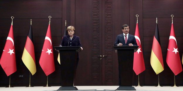 ein Mann und eine Frau stehen jeweils an einem Pult neben deutschen und türkischen Fahnen