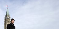 Justin Trudeau vor im scharzen Mantel vor einem Turm und einem weiten, leeren, blau-weißen Himmel
