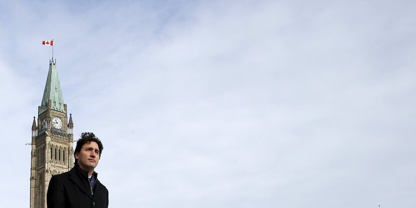 Justin Trudeau vor im scharzen Mantel vor einem Turm und einem weiten, leeren, blau-weißen Himmel