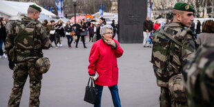 Eine ältere Dame in Rot zwischen zwei Soldaten auf den Champs-Élysées in Paris