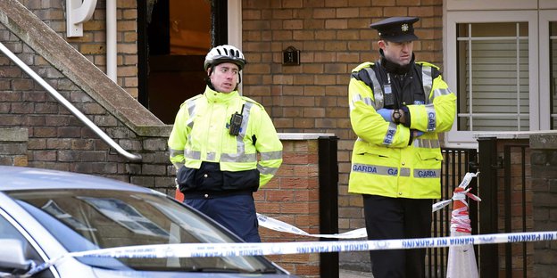 Zwei Polizist_innen in neonfarbenen Jacken sichern einen Hauseingang.