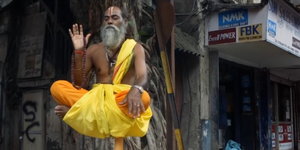 Zwei mit orangfarbenn und gelben Tüchern bekleidete Inder sitzen meditierend auf der Straße