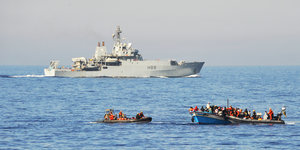Bundeswehrsoldaten in Speedbooten übernehmen Flüchtlinge. Im Hintergrund ein britisches Schiff.