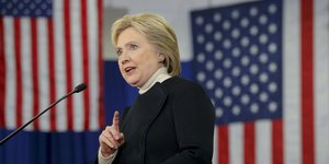 Clinton redet mit erhobenem Zeigefinger vor US-amerikanischen Flaggen