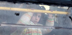Ein junges syrisches Mädchen guckt traurig aus einem Busfenster