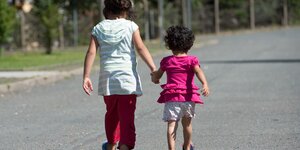 Zwei Kinder laufen Hand in Hand, ihren Rücken dem Fotografen zugewandt