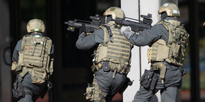 Drei uniformierte und vollgepanzerte Polizisten laufen mit Maschinengewehr in den Händen in einen Hauseingang.