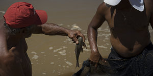 Ein Mann zieht einen Fisch aus dem schlammbraunen Wasser