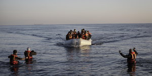 Ein Schlauchboot mit Flüchtlingen in Rettungswesten fährt auf Menschen zu, die im Wasser stehen