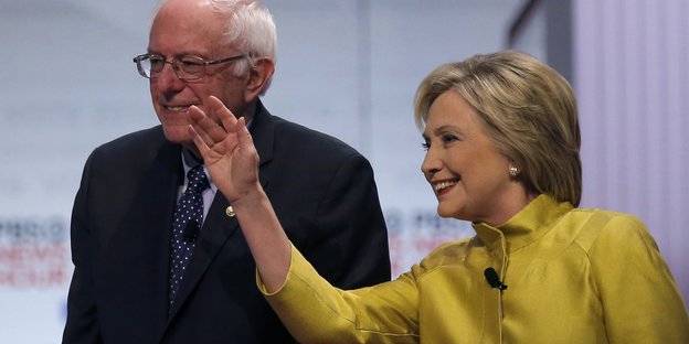 Bernie Sanders und Hillary Clinton stehen nebeneinander, Clinton winkt