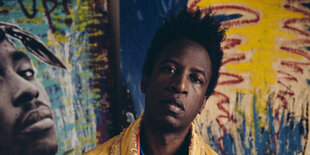 Saul Williams vor einem Wandbild, das Tupac zeigt