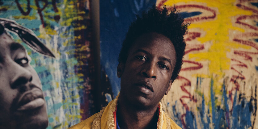 Saul Williams vor einem Wandbild, das Tupac zeigt