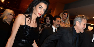 Links im Bild ist Amal Clooney, rechts ihre Ehemann. Im Hintergrund sind weitere Personen zu sehen