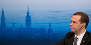 Medwedew alleine vor einem blauen Hintergrund mit der Silhouette von München.