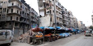 Eine Häuserfront in Aleppo. Auf der Straße Stände mit Obst und Gemüse.