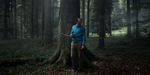 Im dunklen Wald steht ein Mann mit Telefonhörer.